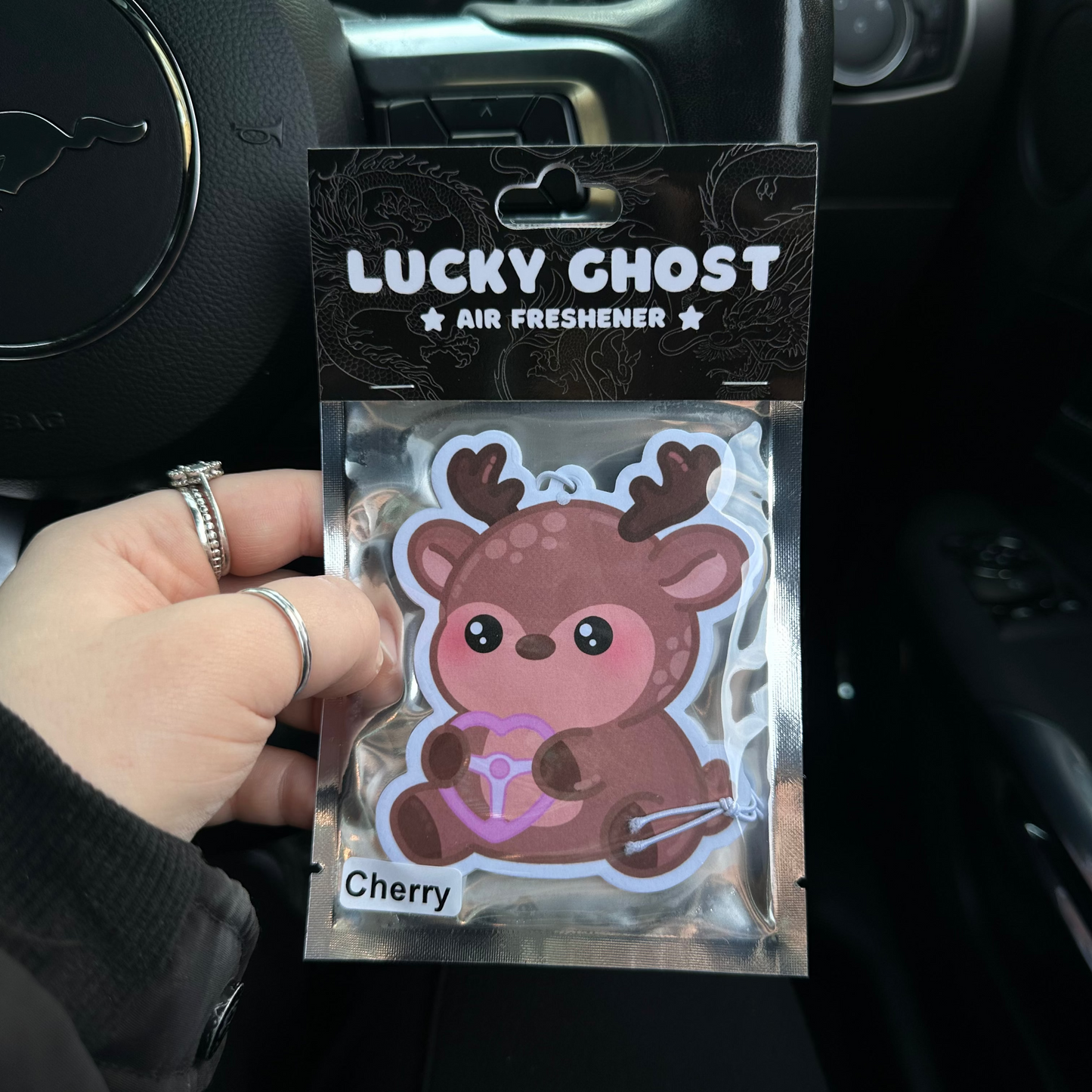 Lucky Ghost air freshener packaging held in front of a car dashboard.