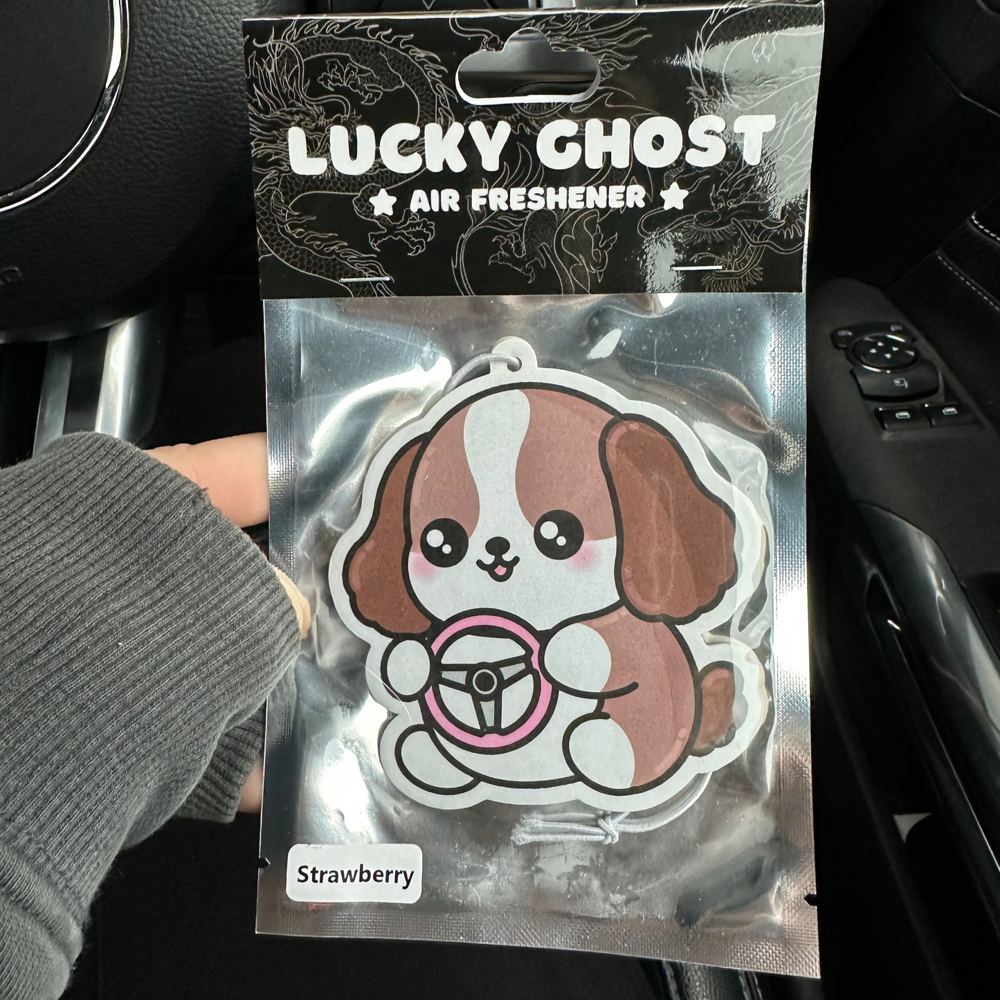 Lucky Ghost air freshener packaging held in front of a car dashboard.