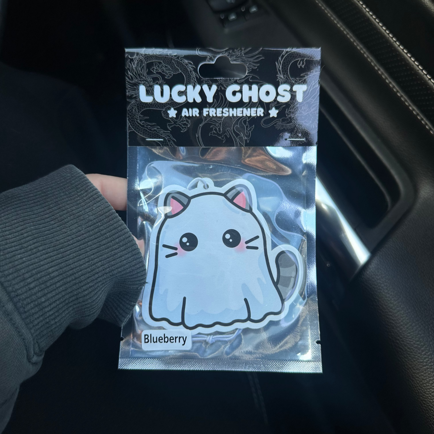 Lucky Ghost air freshener packaging held in front of a car interior.