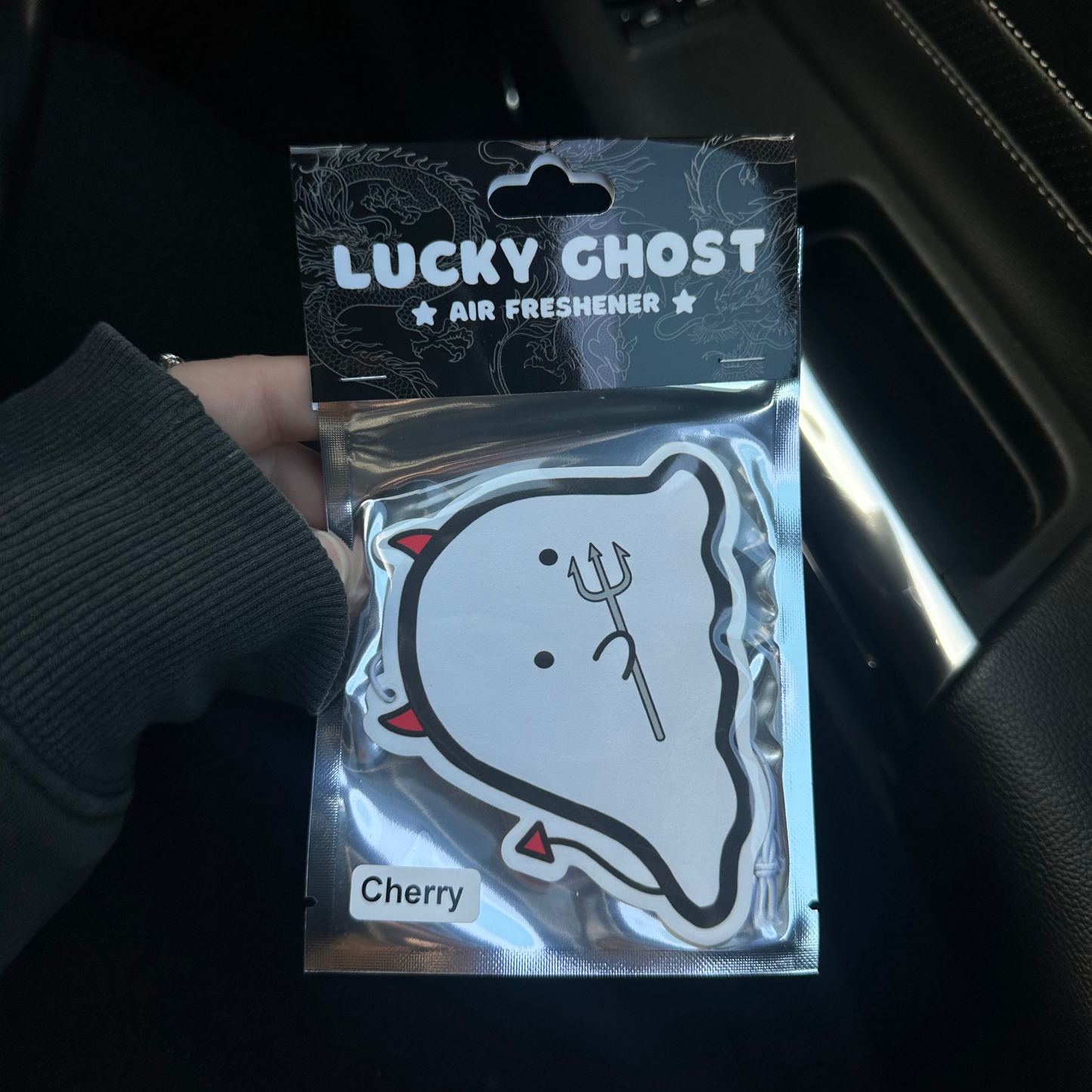 Lucky Ghost air freshener packaging held by a person inside a car.