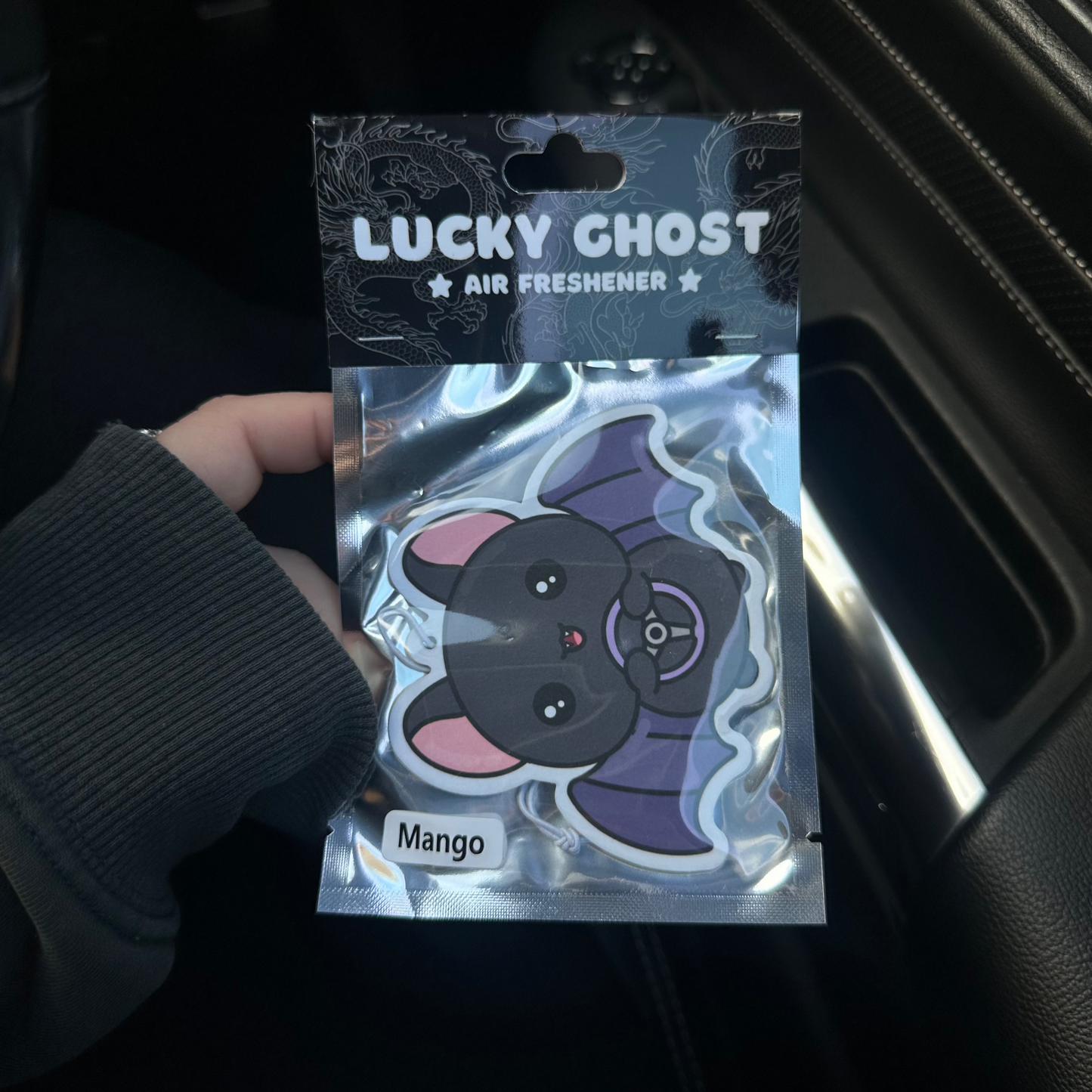 Lucky Ghost air freshener packaging held by a person inside a vehicle.