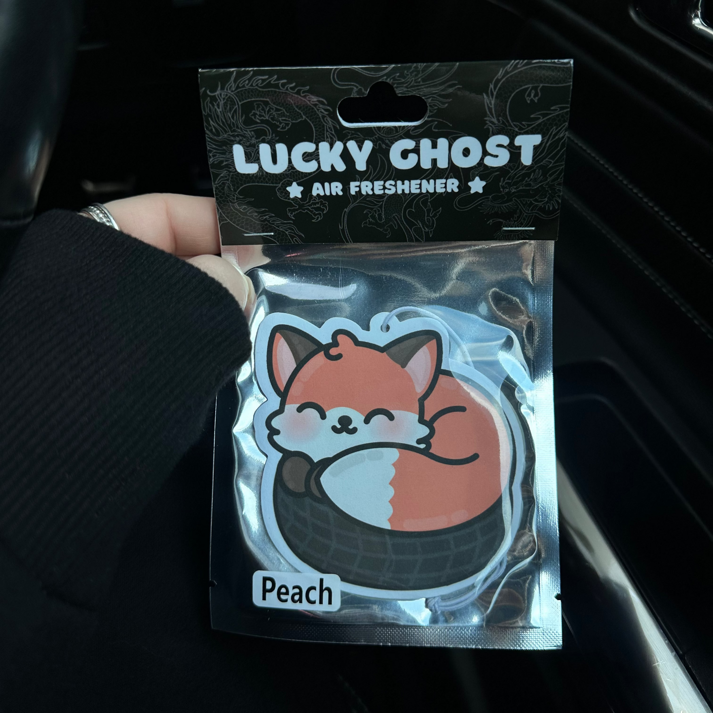 Lucky Ghost air freshener packaging with a fox design held in front of a car interior.
