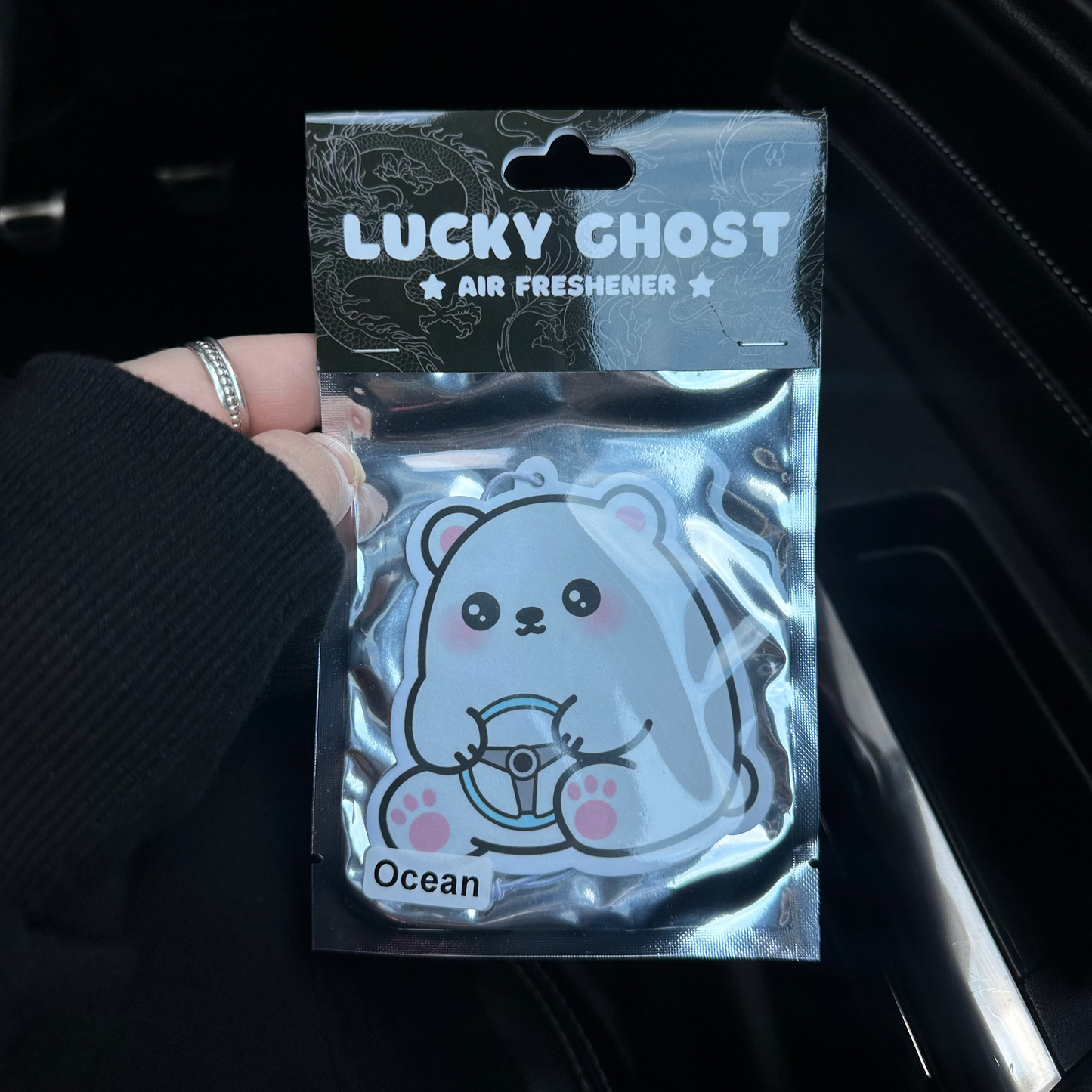 Lucky Ghost air freshener packaging held by a person in a dark car interior.