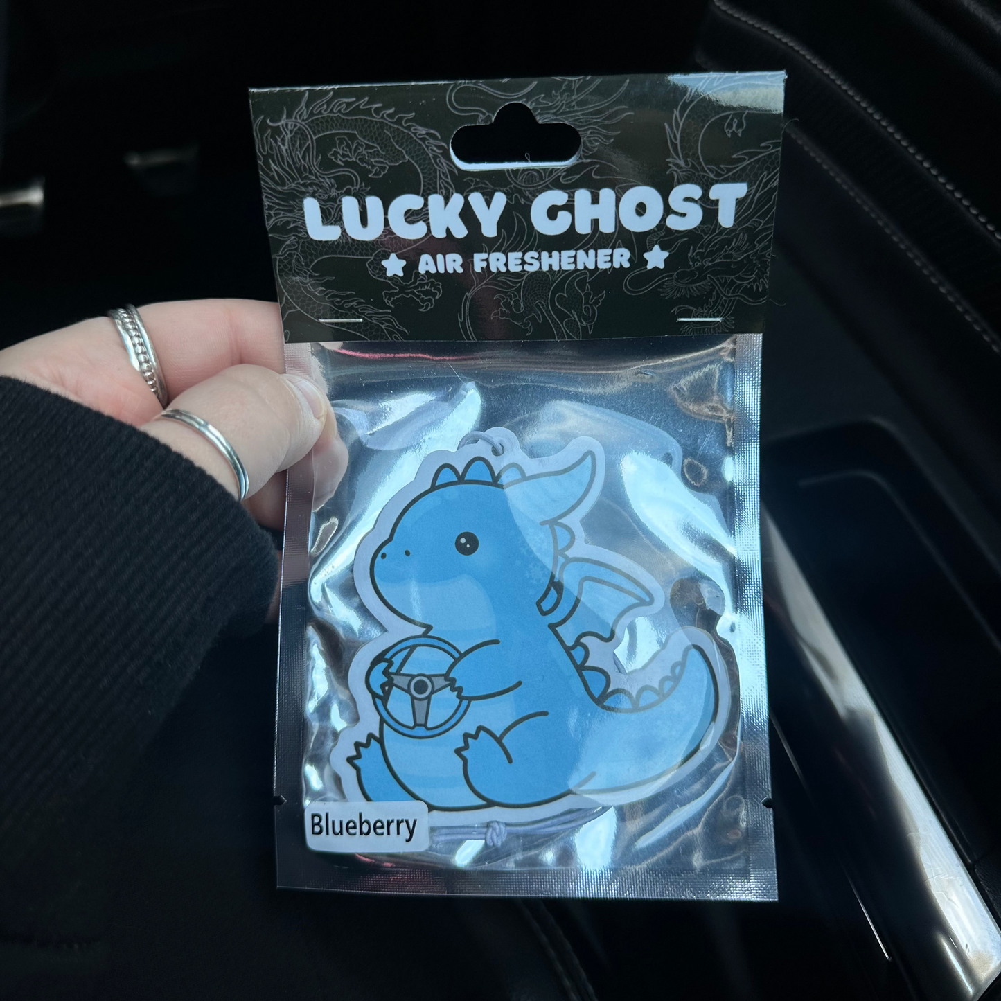 Lucky Ghost air freshener packaging with a blue dragon design held in front of a car interior.