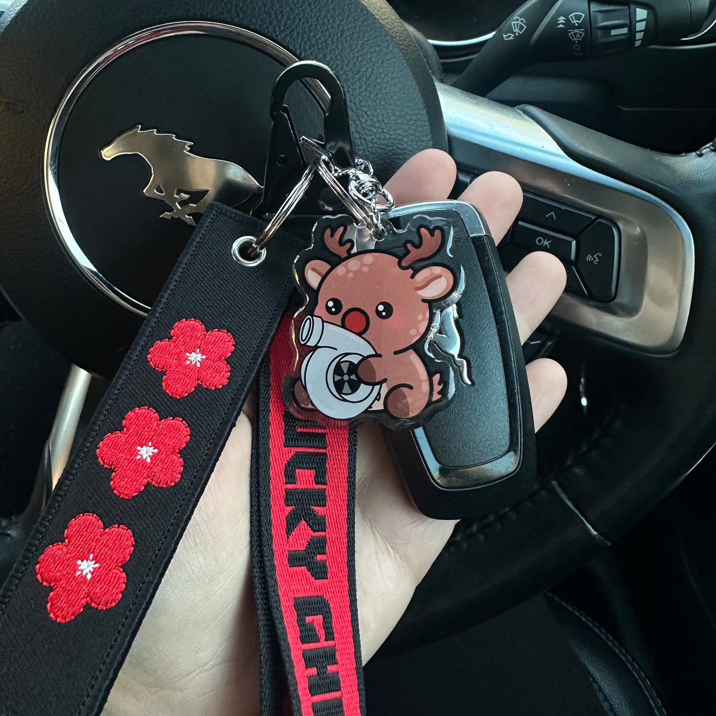 Keychain with a bear charm and red floral designs on a strap, held in front of a car's dashboard.