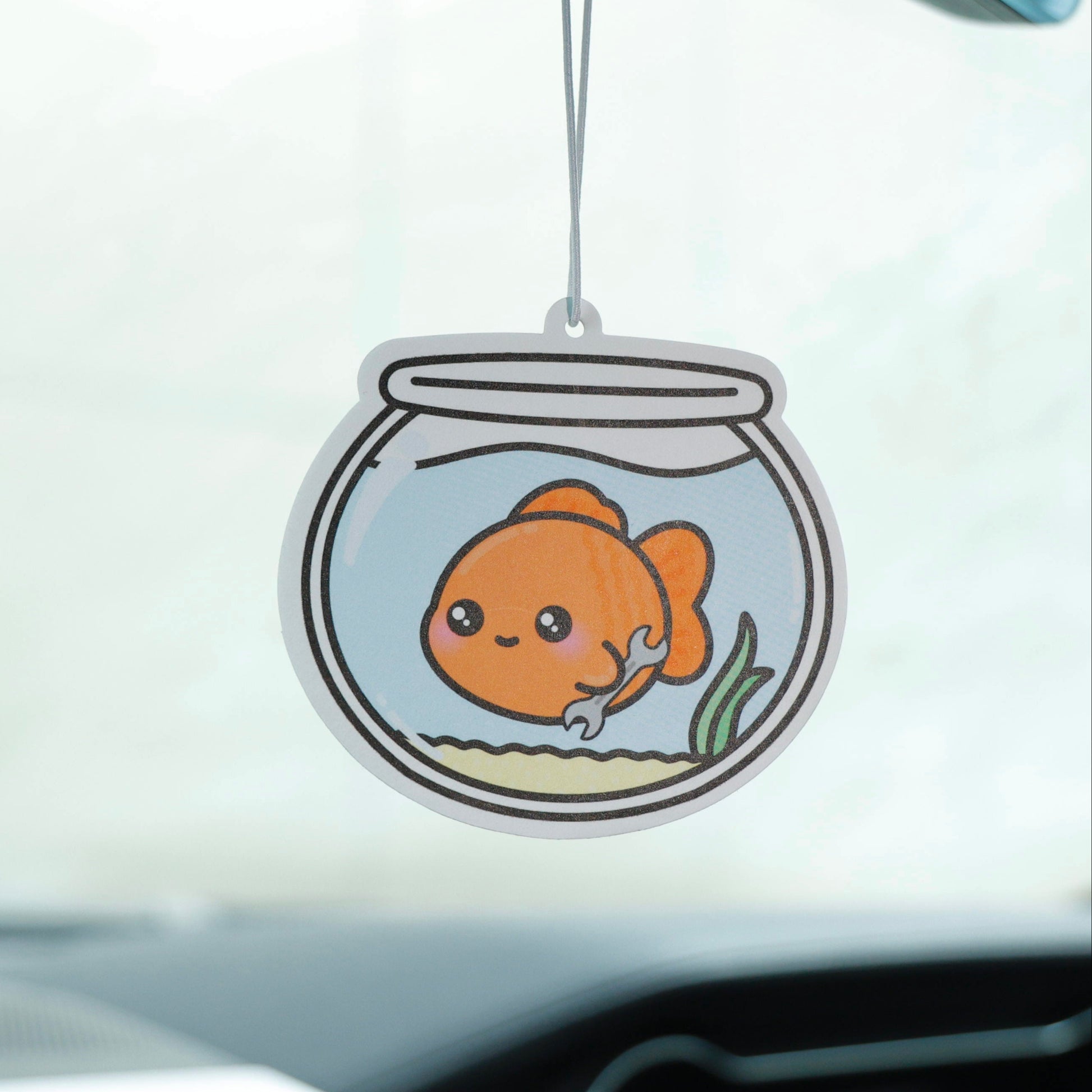 Car air freshener with a goldfish design hanging from a car's dashboard.