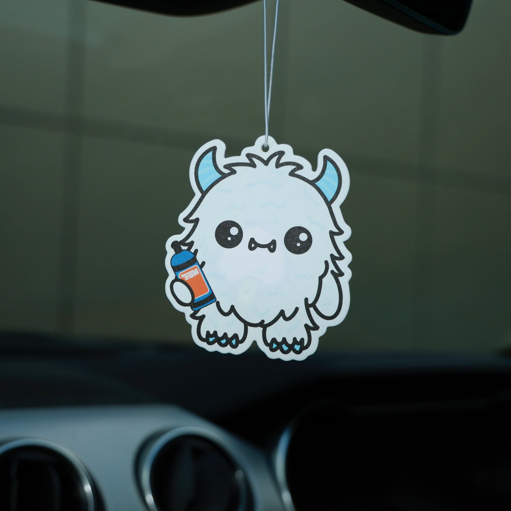 Car air freshener with a cute monster design hanging from a car's rearview mirror.