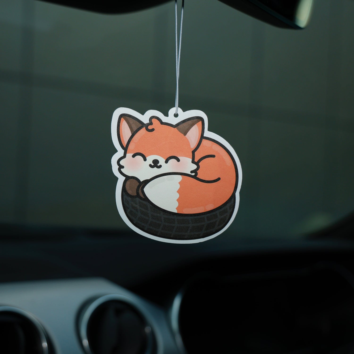 Car air freshener shaped like a fox hanging from a car's rearview mirror.
