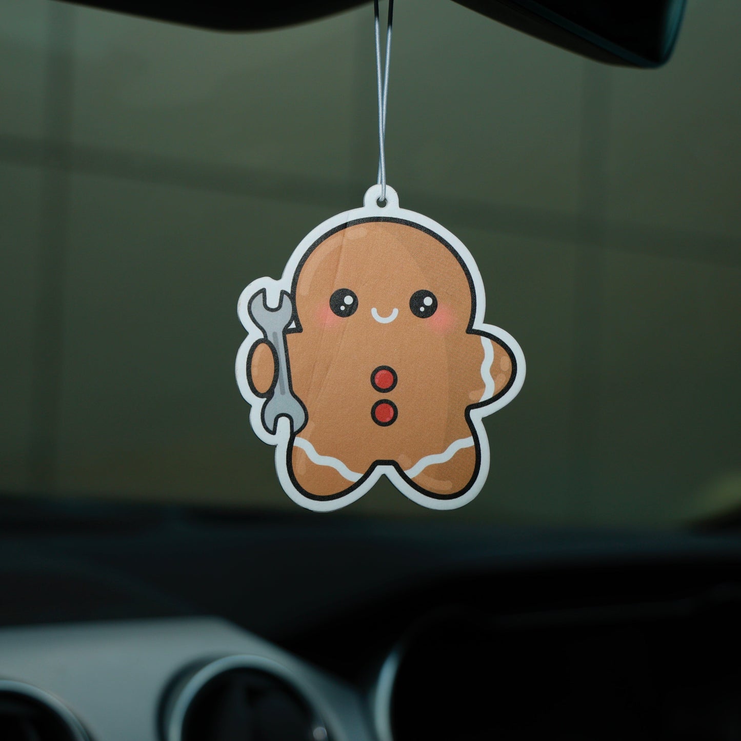 Car air freshener shaped like a gingerbread man hanging from a car's rearview mirror.