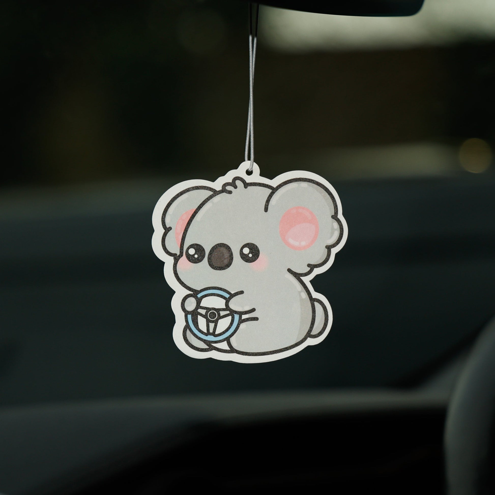 Car air freshener shaped like a cartoon koala hanging from a car's rearview mirror.
