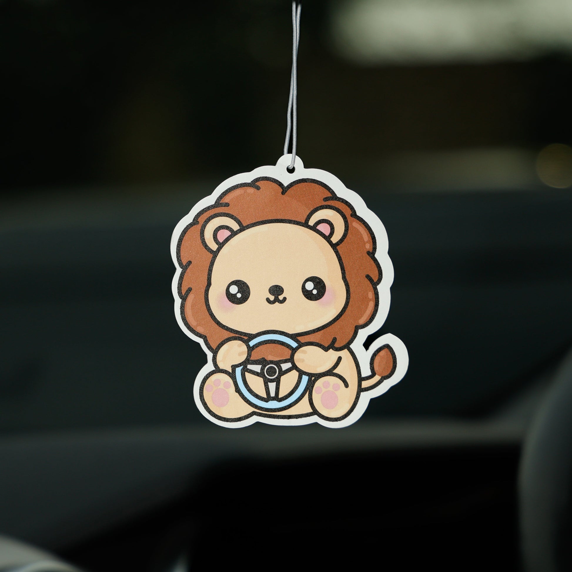 Car air freshener shaped like a lion hanging from a car's rearview mirror.
