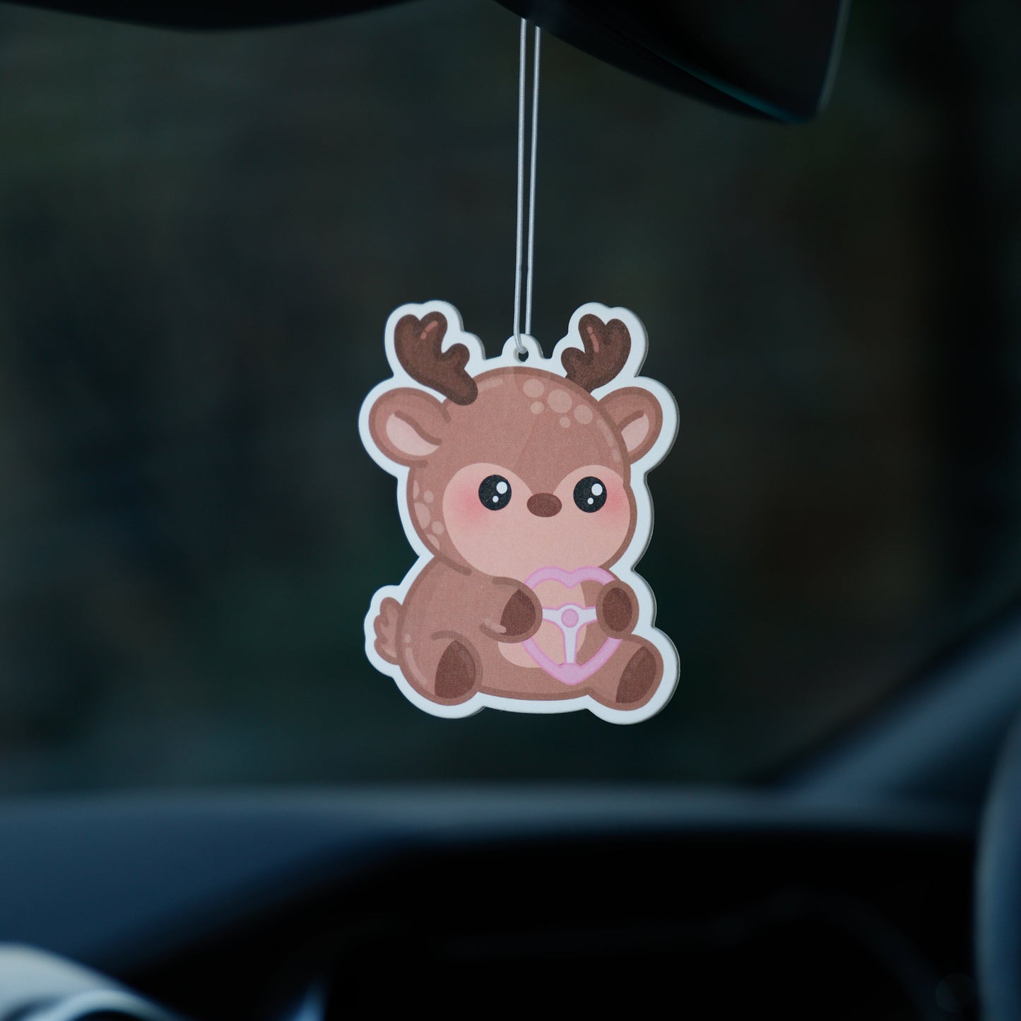 Car air freshener shaped like a cartoon deer hanging from a car's rearview mirror.