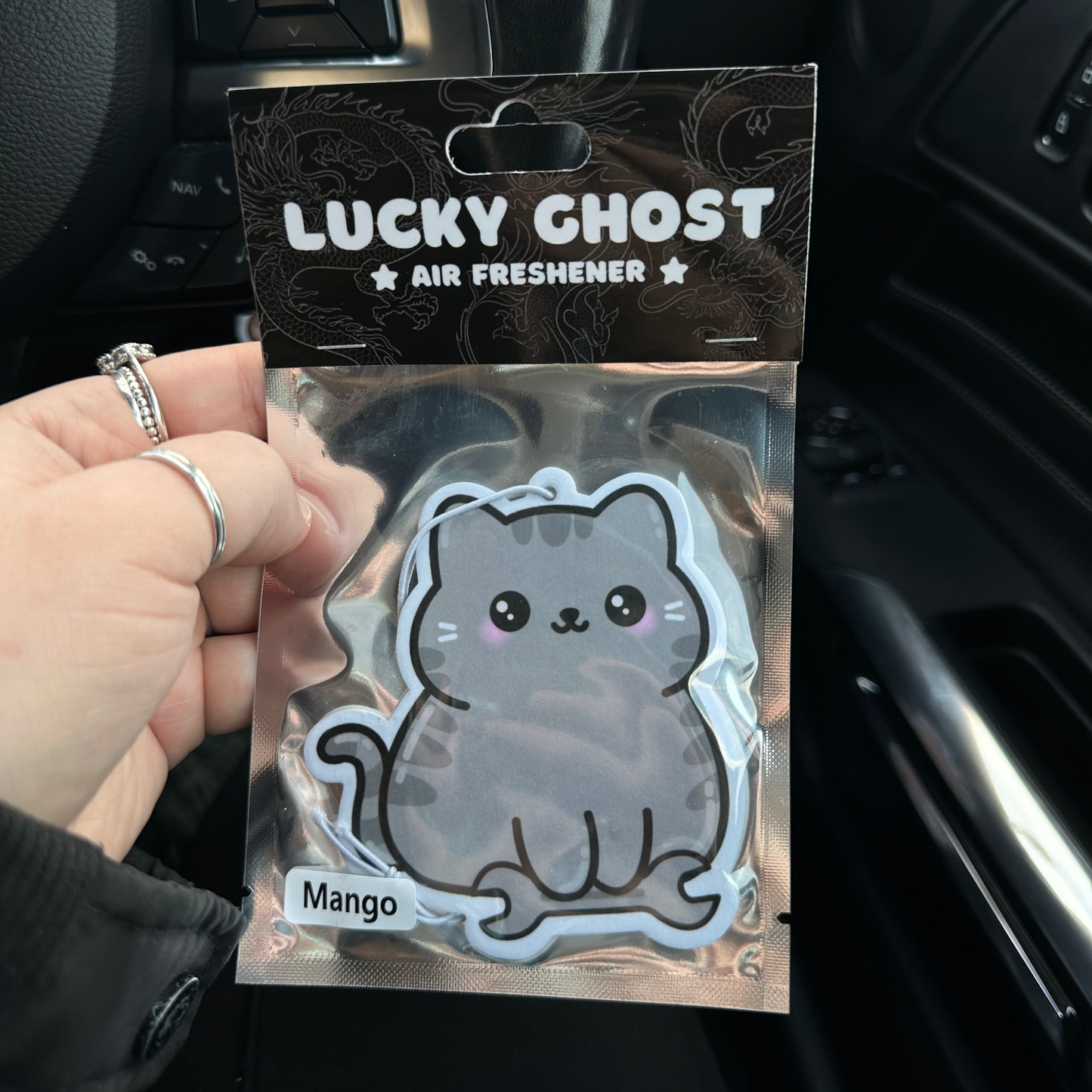 Lucky Ghost air freshener packaging held by a hand inside a car.