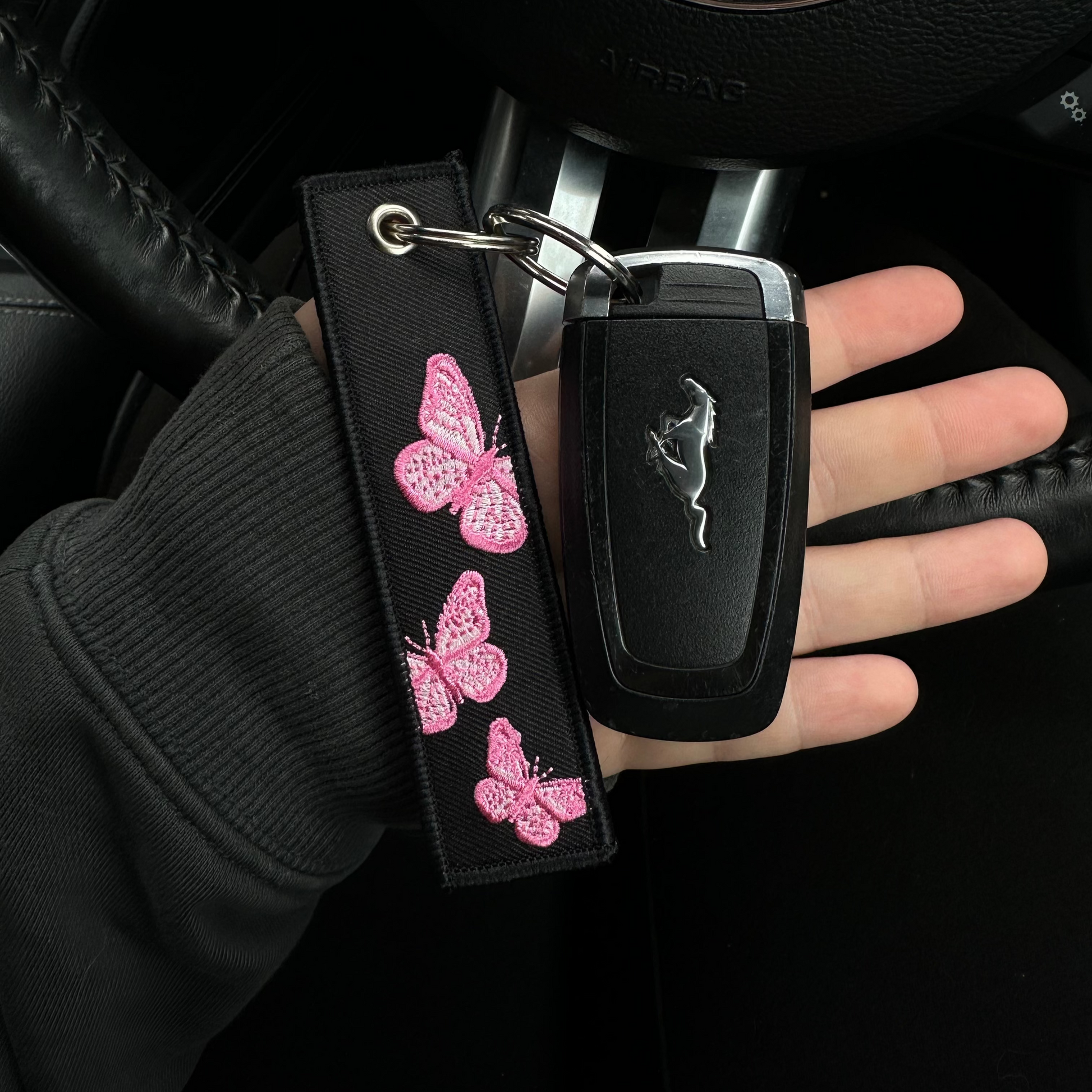 Car key with butterfly design keychain held by a hand inside a car.