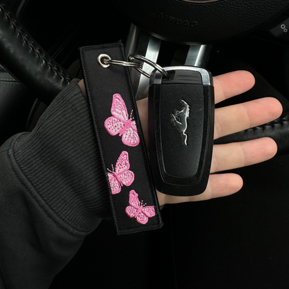 Car key with butterfly design keychain held by a hand inside a car.