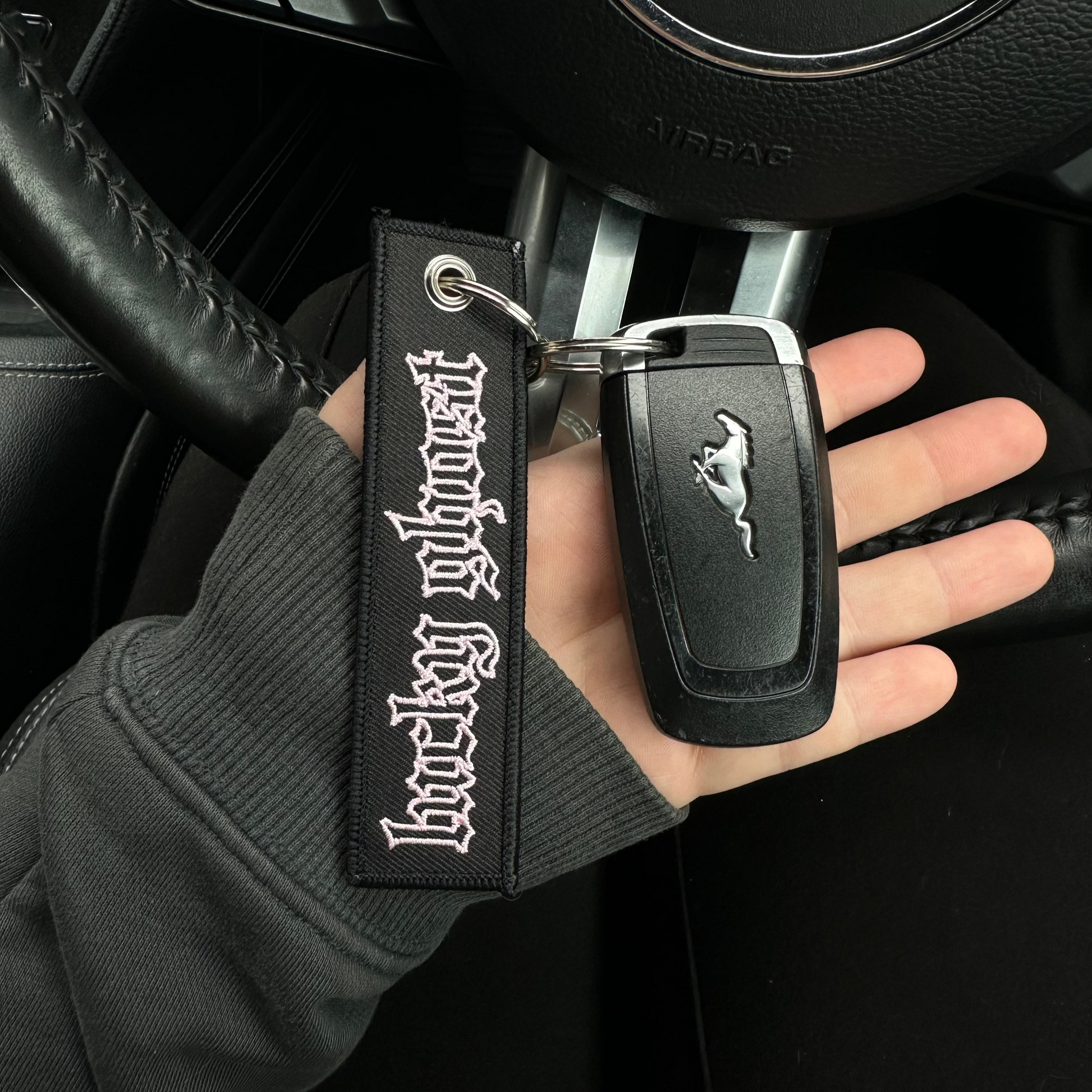 Hand holding a car key with a keychain featuring a logo, inside a vehicle.