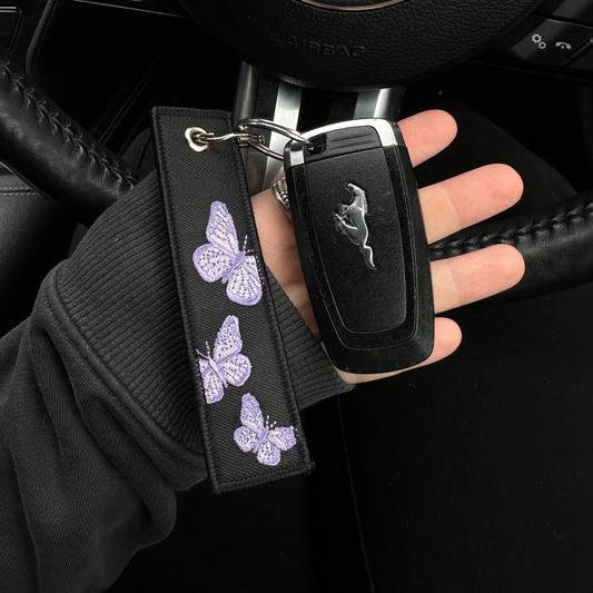 Car key with butterfly design keychain held by a hand inside a car.