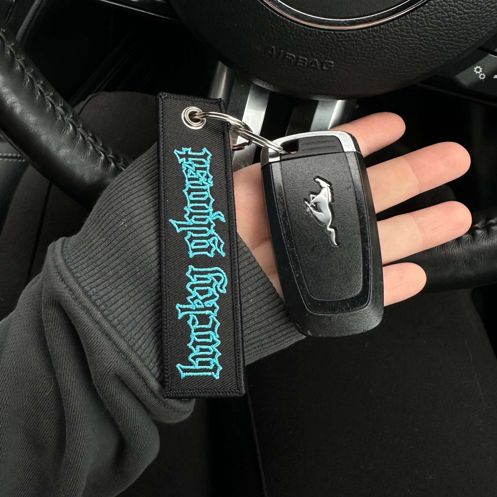 Hand holding a car key with a keychain featuring a logo, inside a vehicle.