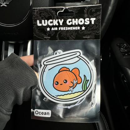 Lucky Ghost air freshener packaging with a goldfish design held by a person inside a car.