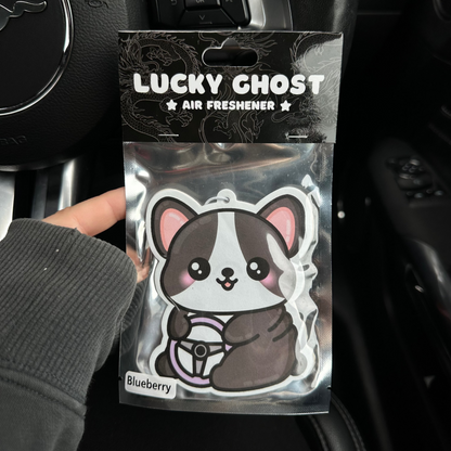 Lucky Ghost air freshener packaging held in front of a car's steering wheel.