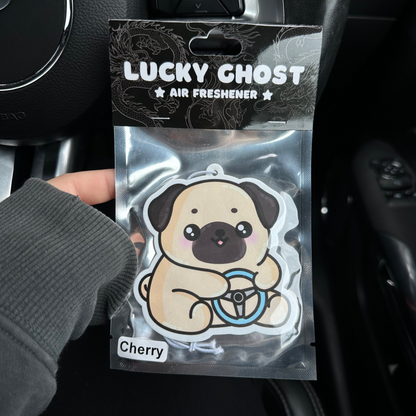Lucky Ghost air freshener packaging with a pug design held in front of a car's dashboard.