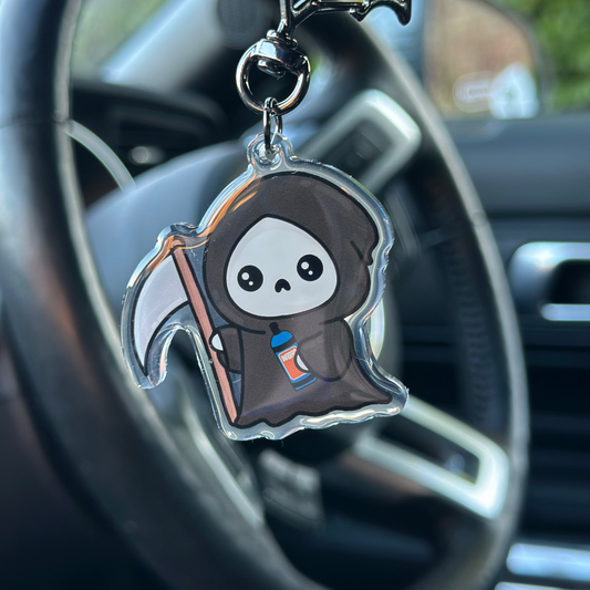 Car air freshener shaped like a cute grim reaper character hanging from a car's rearview mirror.