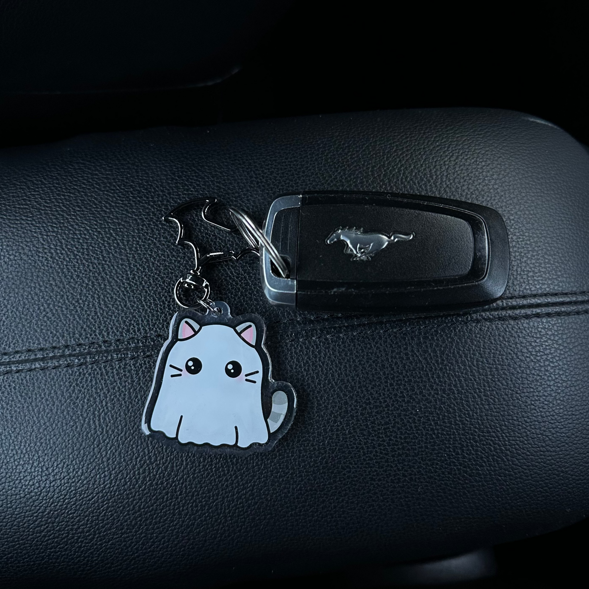 Cat-shaped keychain attached to a car's key holder on a black leather car interior.