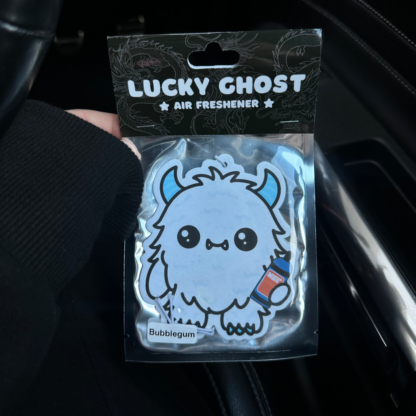 Lucky Ghost air freshener packaging held in a car interior