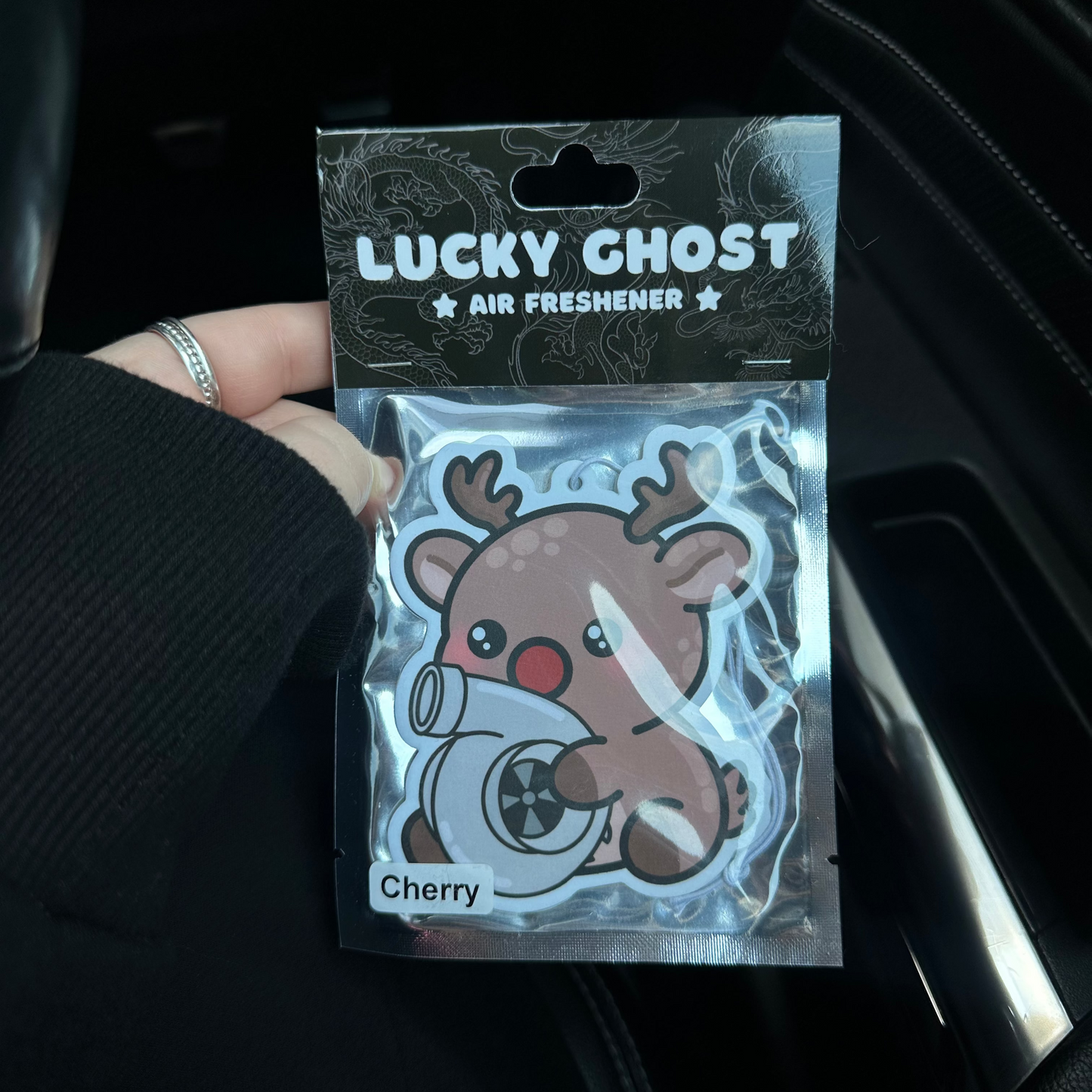 Lucky Ghost air freshener packaging held by a person in a car.