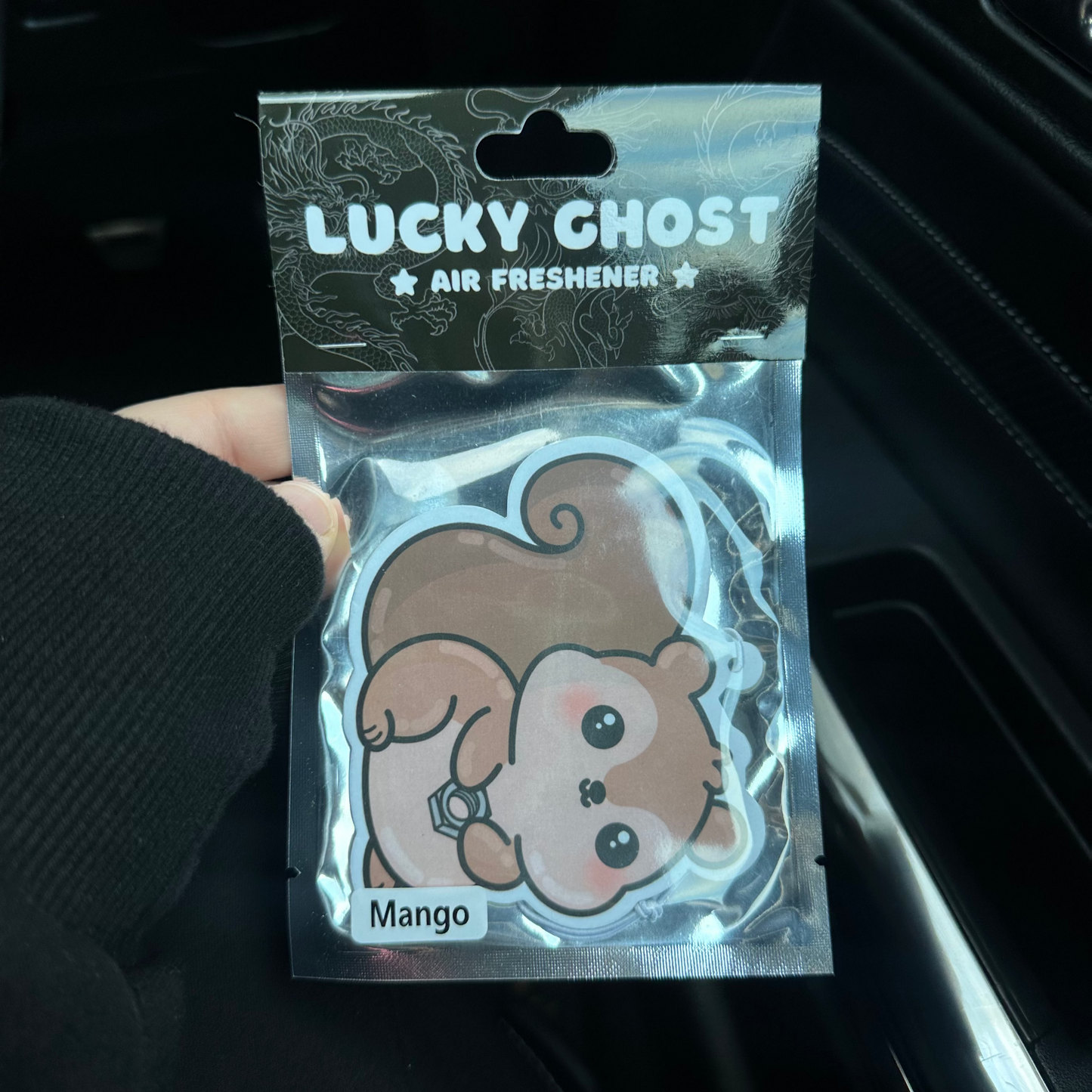 Lucky Ghost air freshener packaging with cartoon ghost design held by a hand.