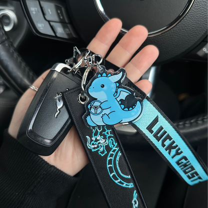 Hand holding a keychain with a blue ghost design in front of a car steering wheel with a Mustang logo.