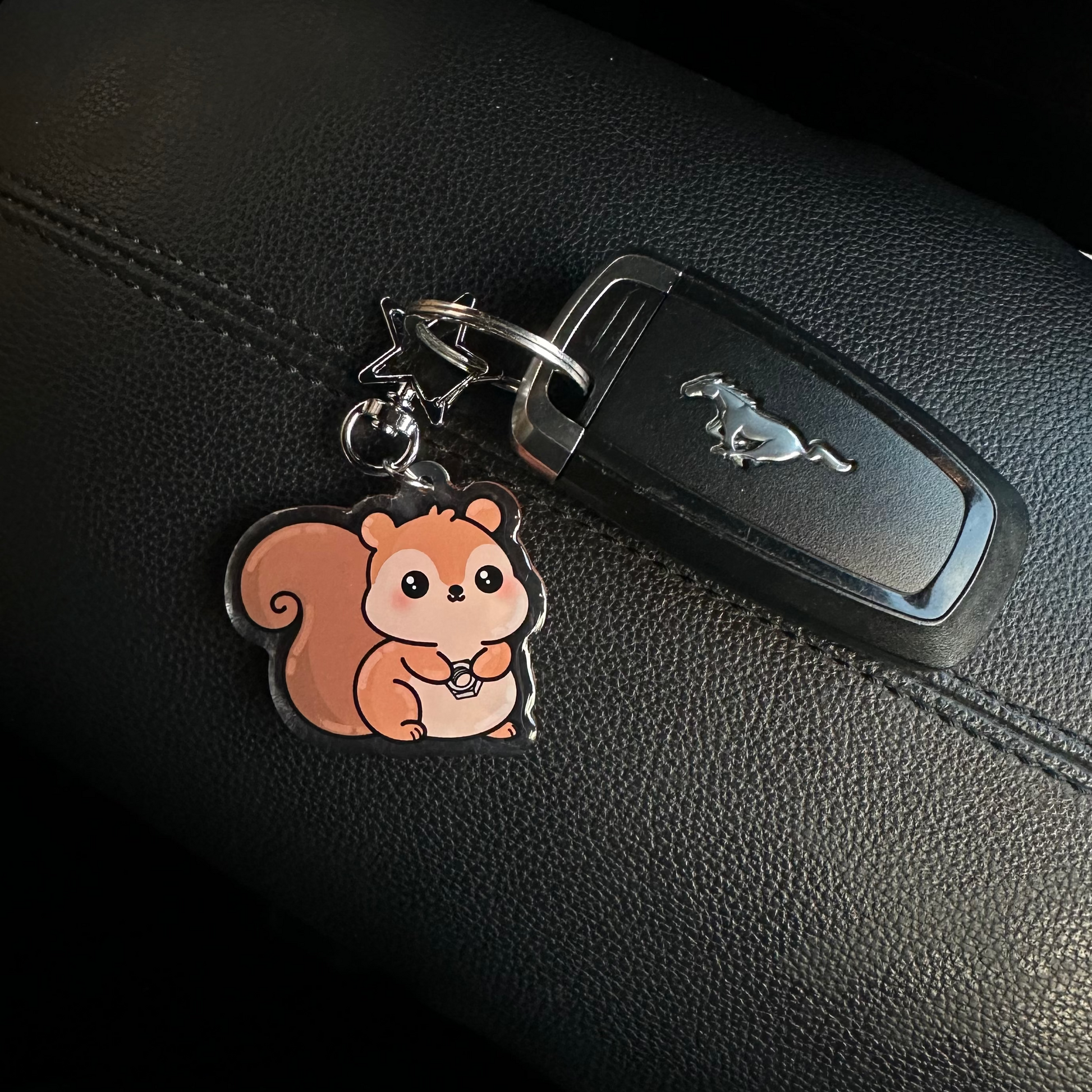 Car keychain with a squirrel design attached to a car key on a black leather surface.