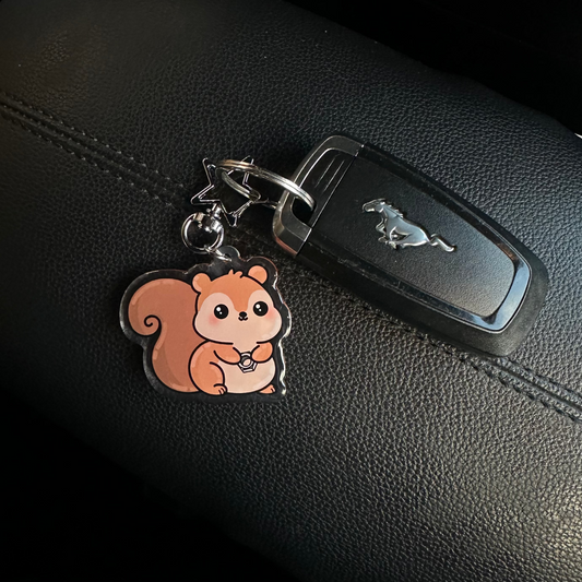 Car keychain with a squirrel design attached to a car key on a black leather surface.