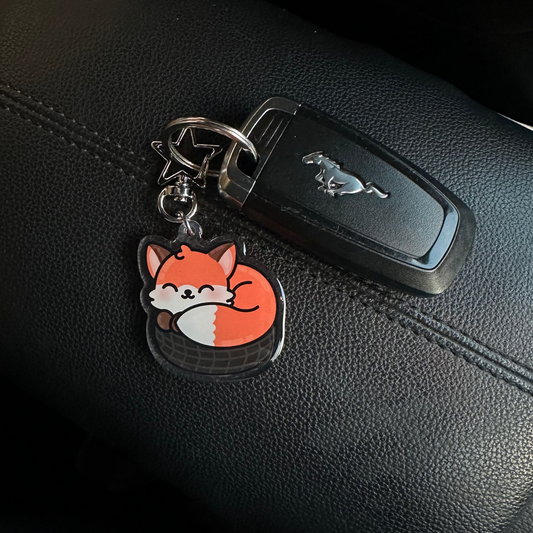 Keychain with a fox design attached to a car key on a black leather surface