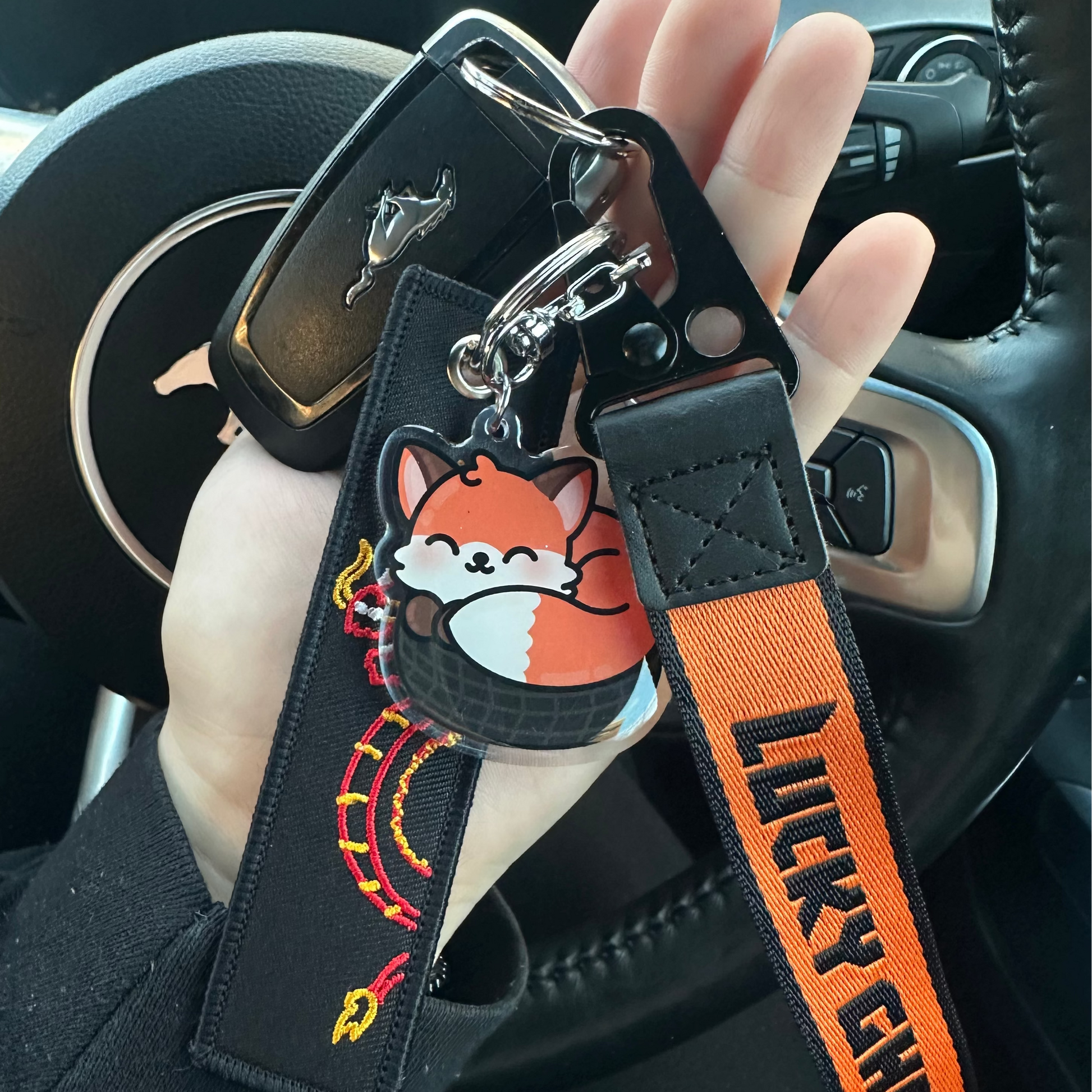 Keychain with fox charm and 'Lucky Ghost' strap held in a car interior.