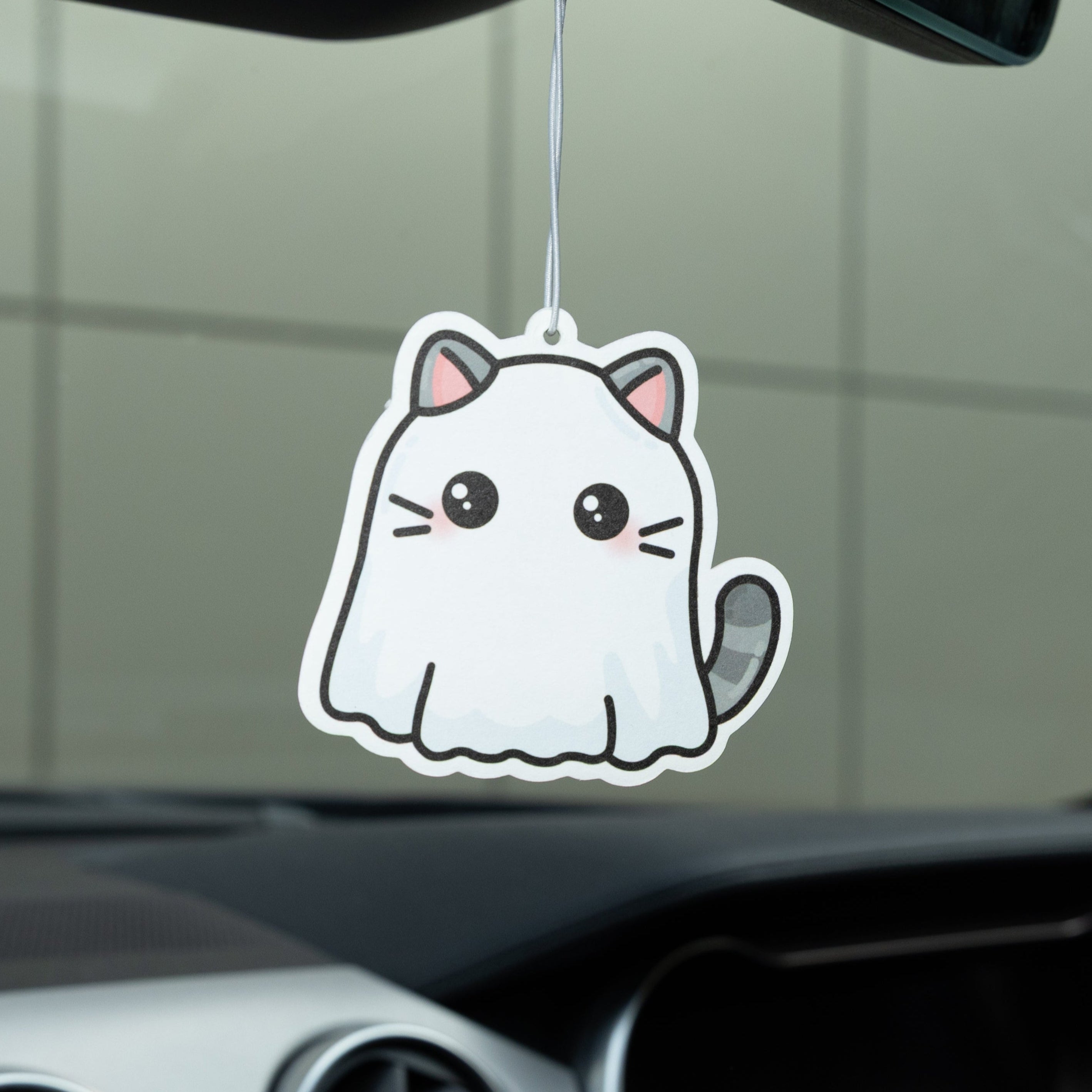 Car air freshener shaped like a cartoon cat hanging from a car's rearview mirror.