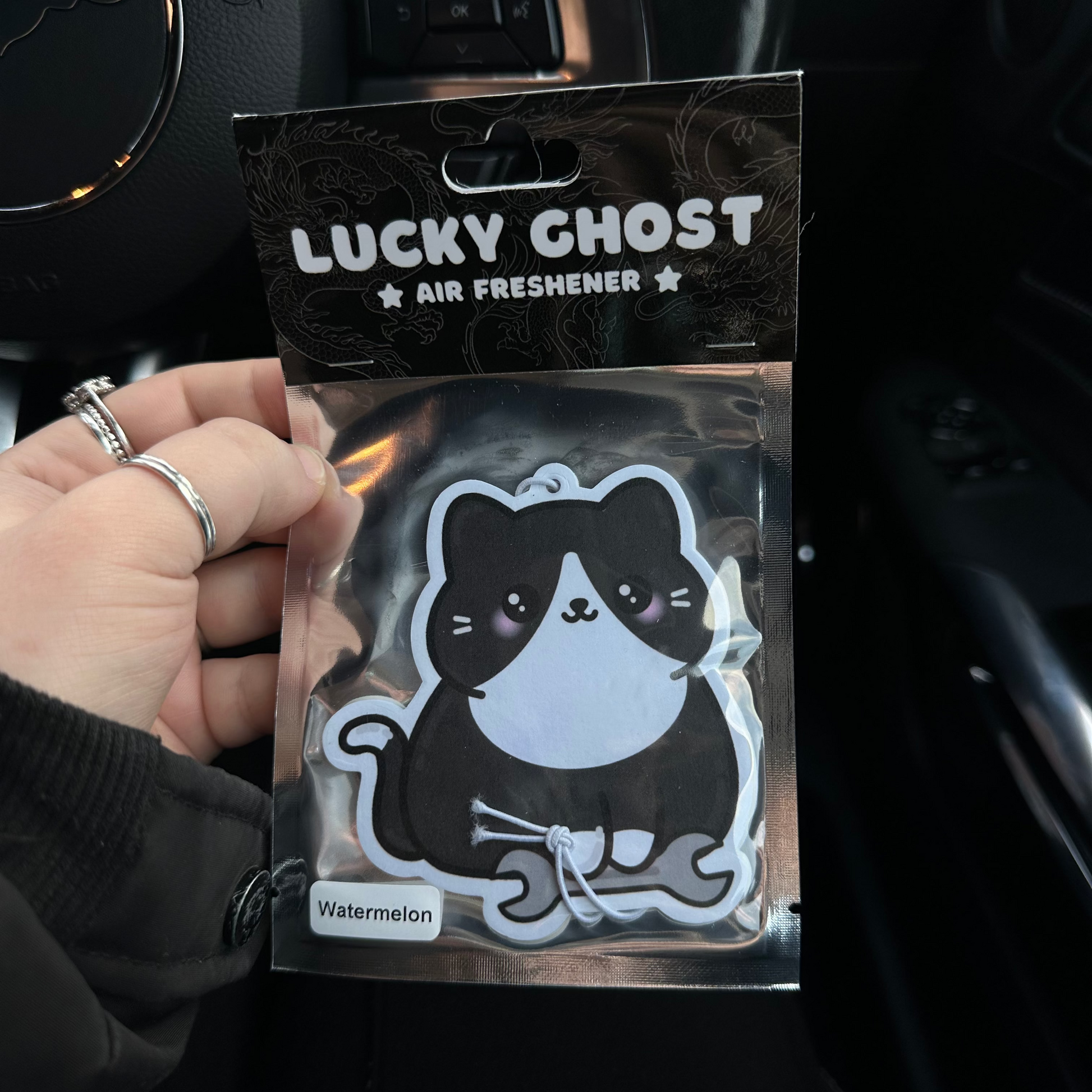 Lucky Ghost air freshener packaging held by a hand inside a car.